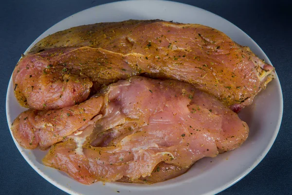 big piece of raw turkey fillet  pickled in spices and herbs lies on white plate against gray background