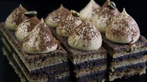 特写全景在三巧克力歌剧蛋糕切片饰以褐色奶油在黑色镜子背景 — 图库视频影像