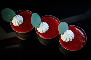 Ahududu panakota tatlı krem ve siyah ayna arka plan üzerinde cam kase otlar ile dekore edilmiş üzerinde Üstten Görünüm