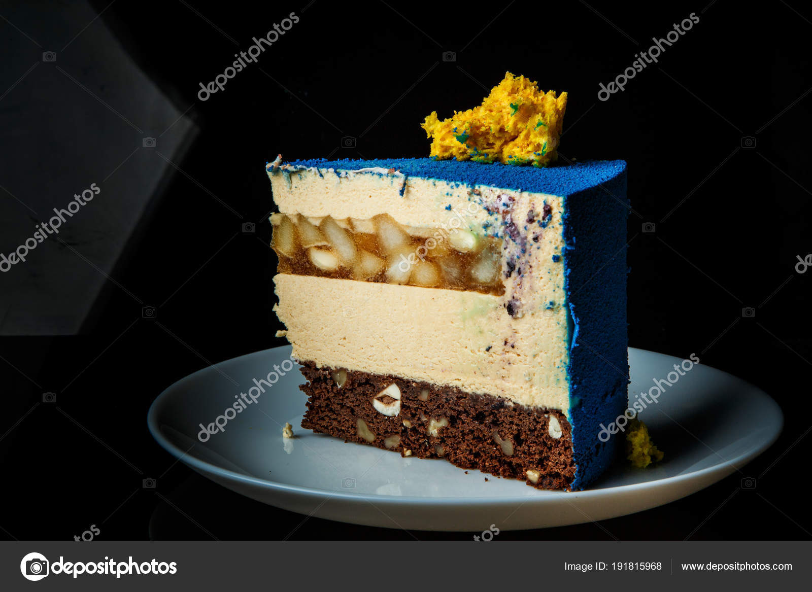 Pezzo di torta mousse blu con decorazione di torta di spugna gialla sul Inter,livello top e caramello pera si trova sulla zolla bianca su sfondo nero\u2013