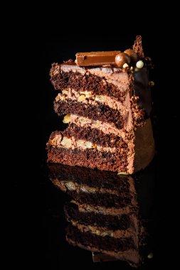 siyah ayna arka plan üzerinde hizmet çikolata şeker krem arası tabaka ile lezzetli çikolatalı kek parçasının dikey görünüm süslenmiş