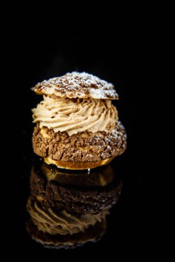 Dikey görünüm üzerinde lezzetli Fransız doldurma karamel kremalı tatlı profiterol siyah ayna arka plan yansıması ile hizmet