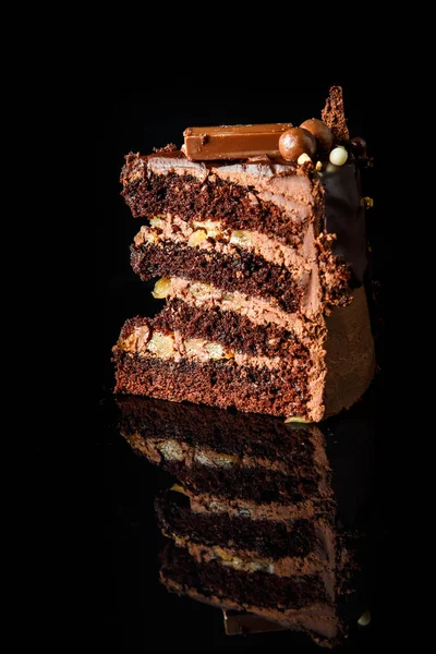 siyah ayna arka plan üzerinde hizmet çikolata şeker krem arası tabaka ile lezzetli çikolatalı kek parçasının dikey görünüm süslenmiş
