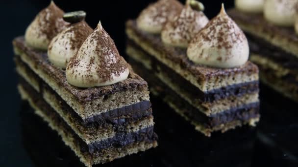 つのチョコレート オペラのクローズ アップ パノラマ ケーキ ブラック ミラーの背景に白いクリームで飾られたスライス — ストック動画