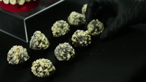 菓子手を置く つの行に黒い背景に砕いたナッツで飾られた丸いボール チョコレートお菓子 — ストック動画