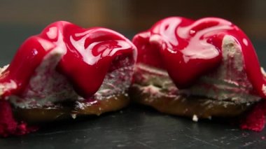 closeup iki kırmızı yarısı hindistancevizi talaşı ile dekore edilmiş ve siyah arka plan üzerinde kırmızı sır ile kaplanmış tatlı mousse