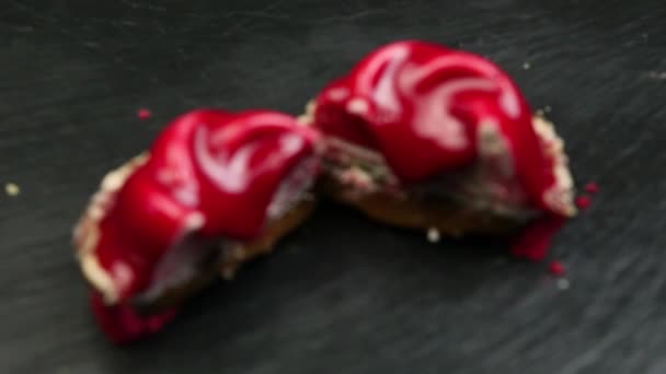 フォーカスの つの赤の半分のムース デザート ココナッツ削りで飾られ 黒の背景に赤い釉薬でコーティング — ストック動画