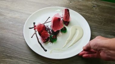 İnsan eli, siyah ahşap masada servis edilen nefis dekore edilmiş lezzetli restoran tatlısıyla beyaz yuvarlak tabağı döndürür.