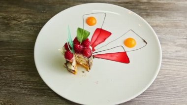 Dilimlenmiş ahududu tatlısını krema ve karamel ile yakınlaştır. Ahşap masadaki beyaz restoran tabağında servis edilir.