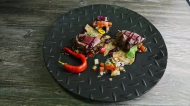 Izgara et parçaları, patates cipsi ve siyah tabakta sebze salatası.