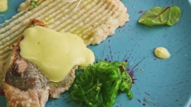 Yakın plan kızarmış balık, sos, patates püresi ve deniz lahanası mavi tabakta döner.