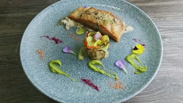 Смачний запечений морський рибний стейк з соусом і смажені овочі обертаються на блакитній тарілці — стокове відео