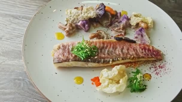 Draufsicht auf trendig dekoriertes gebratenes Fischfilet mit Gemüsescheiben rotiert auf Teller — Stockvideo