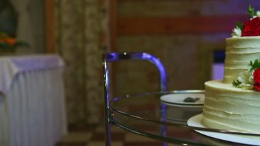 Büyük bir ziyafet salonunda cam tepside servis edilen kırmızı güllerle süslenmiş iki katlı beyaz düğün pastasında yavaş bir panorama.