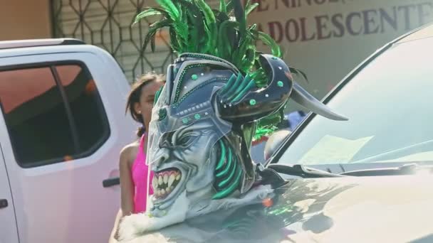 Dominican κορίτσι περπατά παρελθόν μεγάλο καρναβάλι δαίμονας μάσκα στέκεται στο αυτοκίνητο κουκούλα — Αρχείο Βίντεο