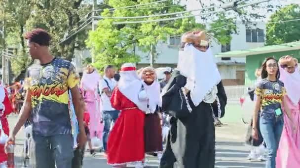 Mensen in lichte carnaval kostuums lopen op dominicaanse stad straat op jaarlijkse evenement — Stockvideo