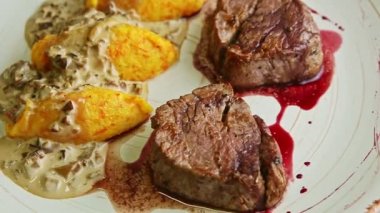 Üst görüntü kırmızı soslu iki parça kızarmış et üzerine yakın plan, modern beyaz restoran tabağında krem mantar sosuyla süslenmiş patates süslemesi.