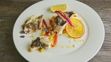 İnsan eli, beyaz tabaktan limon dilimi ve yarısı yenmiş balık alır.