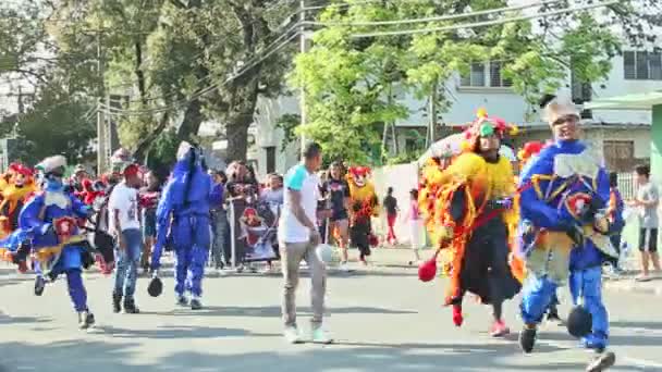 Jóvenes dominicanos con múltiples disfraces de carnaval corren en la calle de la ciudad en el desfile anual — Vídeos de Stock