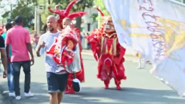 Citizens in fearful red demons costumes walk on city street at dominican carnival — стокове відео