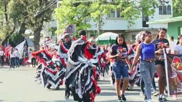 Zoom in at humans in vivid costumes pass on dominican city street at annual carnival — ストック動画