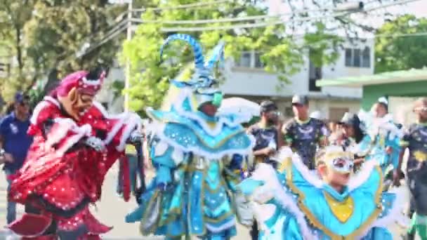 Dominican citizens in sundry carnival costumes pass by on city street at annual parade — 图库视频影像