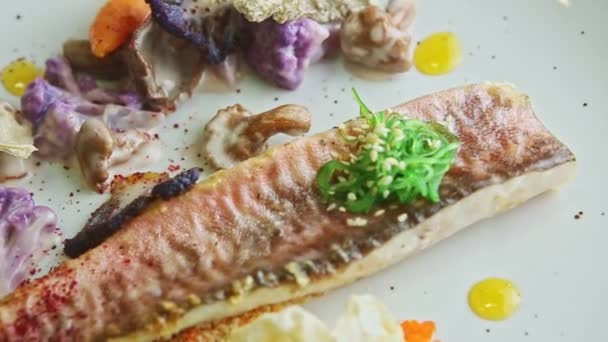 Closeup exquisite decorated grilled fish fillet with vegetables rotates on plate — Stockvideo