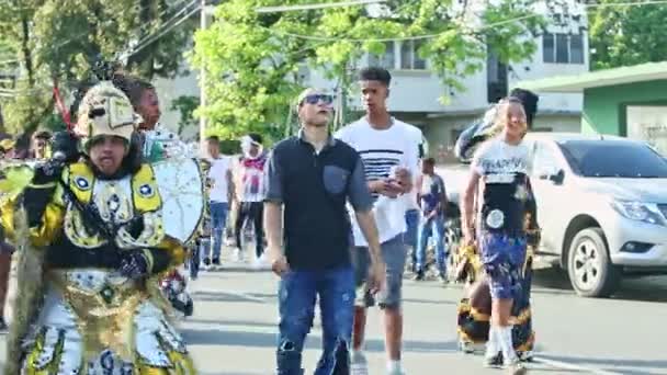 People in diversified carnival costumes walk on city street at dominican festival — ストック動画