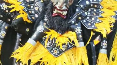 man in bright carnival costume dance at camera on city street at dominican festival