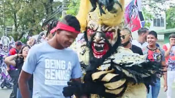 Люди в разнообразных карнавальных костюмах прогуливаются по городской улице на Доминиканском фестивале — стоковое видео