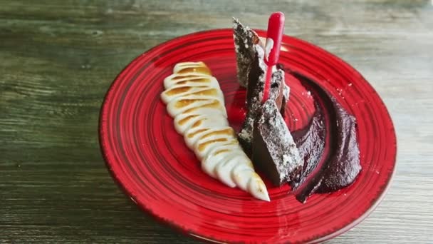 Top view on finely decorated sliced brownie cake with cream rotates on red plate — Stock Video