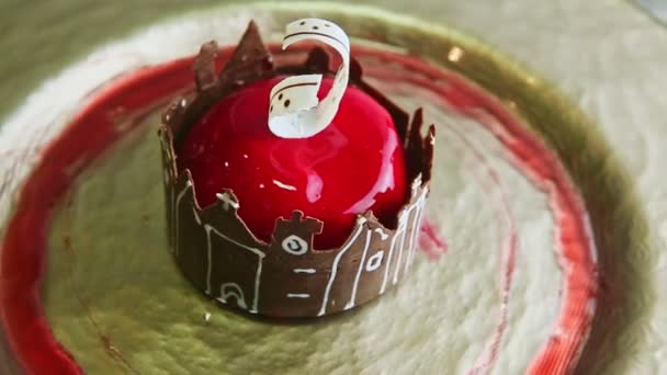 Zooma ut från röd glaserad dessert med slott form choklad roterar på gyllene platta — Stockvideo