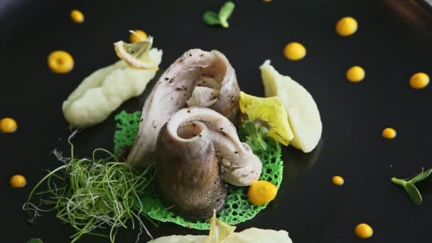 Closeup human hand cuts fish with knife and fork on black plate — 비디오