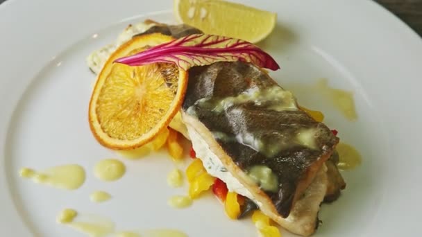 Slow zoom out from finely decorated baked sea fish on sliced peppers on white plate — 비디오