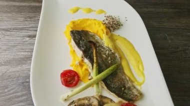 Lezzetli kızarmış deniz balığı filetosu patates püresi ve dilimlenmiş sebzeler tabakta dönüyor.