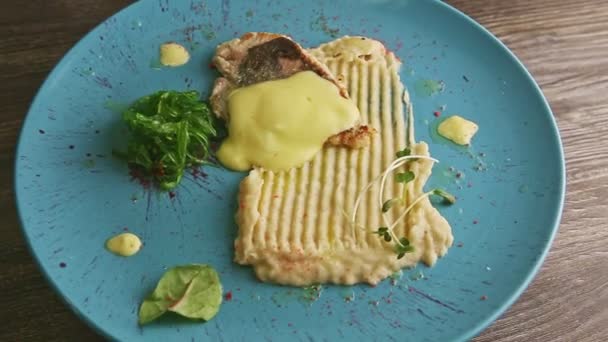 Delicious fried fish fillet with sauce, mashed potato, and sea kale rotates on blue plate — 비디오