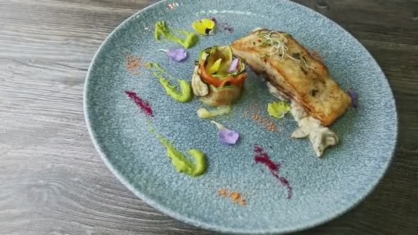 Smaczny pieczony stek rybny z sosem i grillowanymi warzywami obraca się na niebieskim talerzu — Wideo stockowe