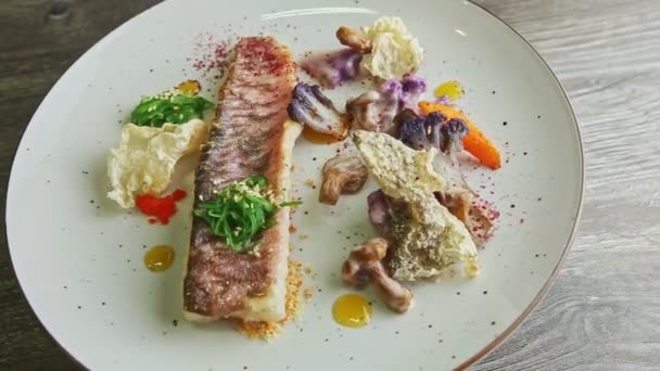 Вид сверху на изысканное украшенное филе жареной рыбы с нарезанными овощами, вращающимися на тарелке — стоковое видео