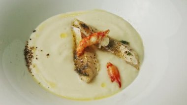 Üst manzara, karides ve kızarmış balık parçalarıyla dekore edilmiş beyaz krema çorbası.