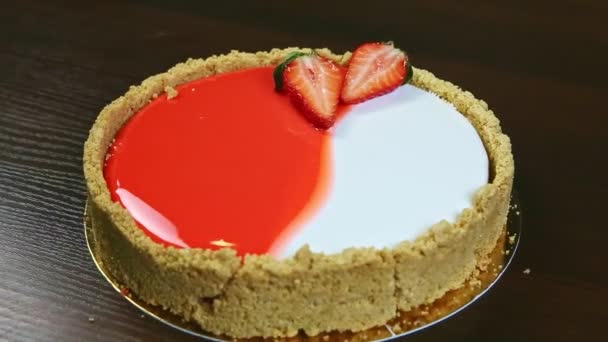 Detailní záběr celý kulatý červený a bílý tvarohový koláč zdobený nakrájenými jahodami — Stock video