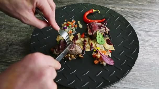 Mänskliga händer skära av liten skiva från rostat kött bit för gaffel och kniv på plattan — Stockvideo