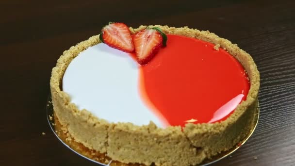 Closeup cheesecake redondo inteiro vermelho e branco decorado com morangos fatiados — Vídeo de Stock