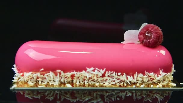 Close-up eclair met roze spiegel glazuur versierd met kokosnoot krullen en framboos — Stockvideo