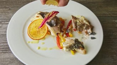 human hand pours by lemon juice chopped stuffed baked fish served on white plate
