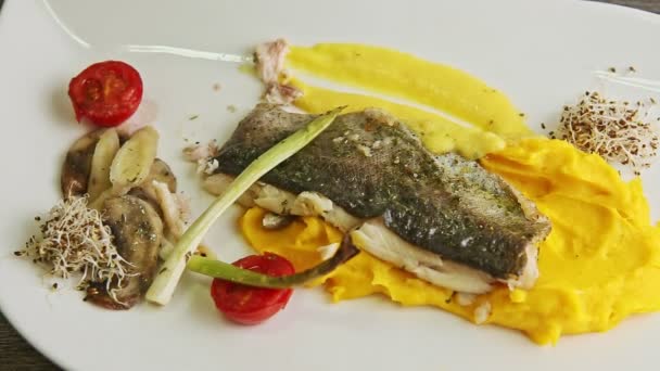 Mãos closeup fatia por faca e garfo frito filé de peixe branco servido com guarnição na placa — Vídeo de Stock