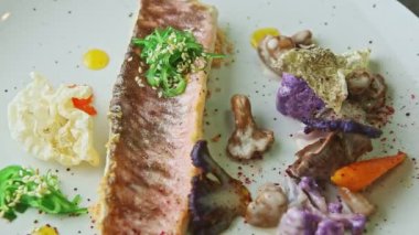 slow zoom out from finely decorated fried fish fillet with vegetables rotates on plate