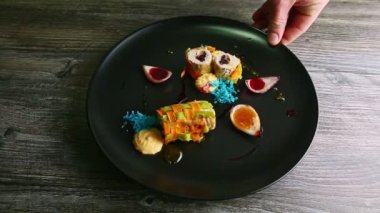 human hand rotates black plate with trendy decorated vegetable stuffed meat rolls