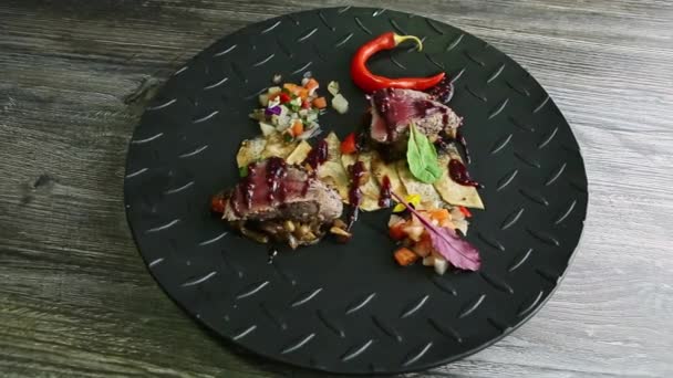 Вид сверху на запеченные куски мяса с картофельными чипсами и овощным салатом на черной тарелке — стоковое видео