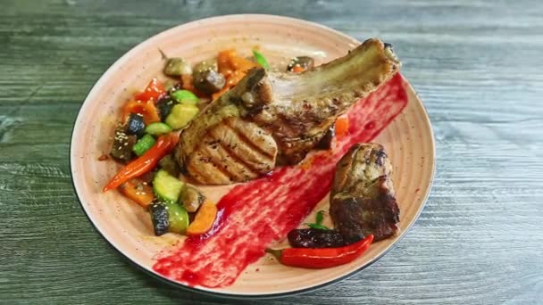 Top view on big baked rib with meat and grilled vegetables rotates on pink plate — 비디오