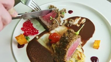 Yakından çekilen eller, çatal ve bıçakla kavrulmuş etten küçük dilimler kesiyor.